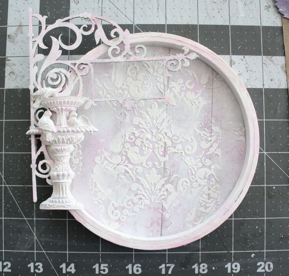 Adhere the the circle of paper to the back of the hoop. Glue the chippy piece to left side hanging over the edge a bit. Adhere the Prima Resin (April Main Kit) piece to the front of the chippy piece.