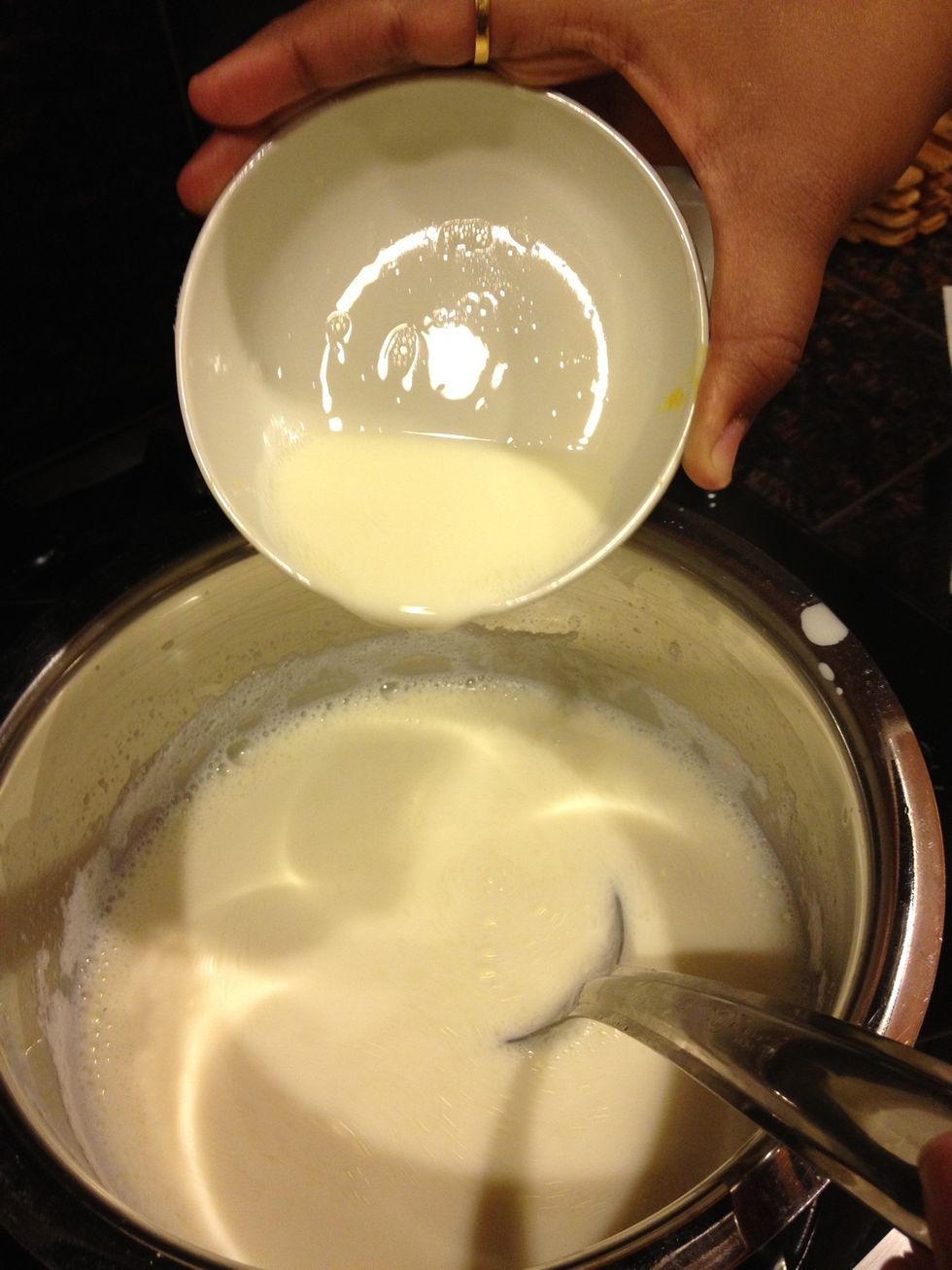 After 15 - 20 minutes, take about two spoons of custard powder and mix it with the boiling milk. Stir the milk while adding the custard powder.