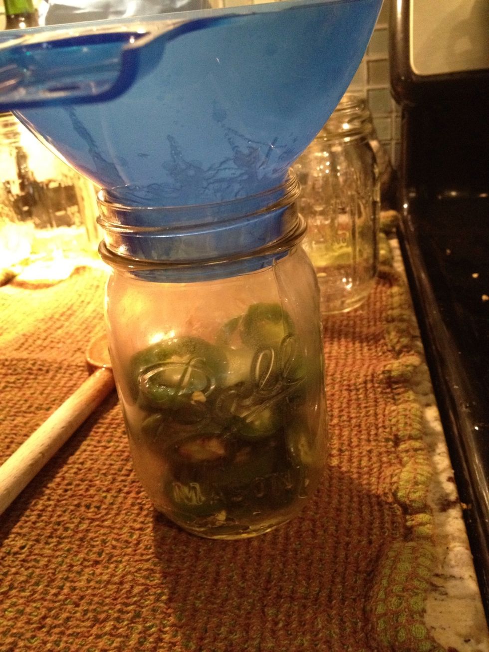 After 4 minutes of simmering the peppers, use a slotted spoon and funnel to transfer the pepper slices into clean, sterile mason jars. Fill the jars to approximately 1/4 inch from the rim.
