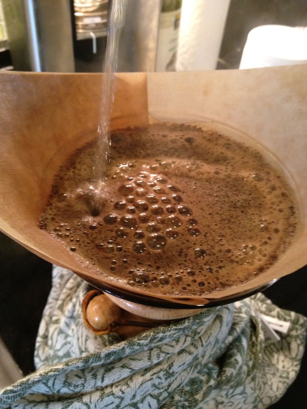 After about a minute pour water slowly and evenly around the grounds.