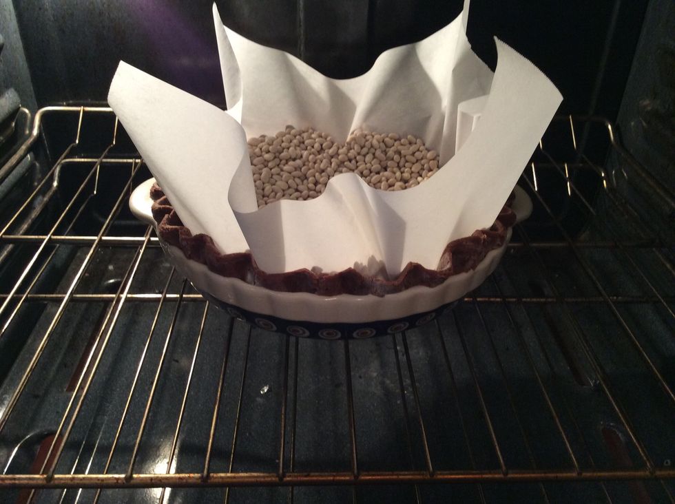 After dough has chilled and the oven is preheated, prepare the pie dough for the oven. Line the pie dough with a piece of parchment paper and fill will dry navy beans, (2lbs). This prevents shrinking.