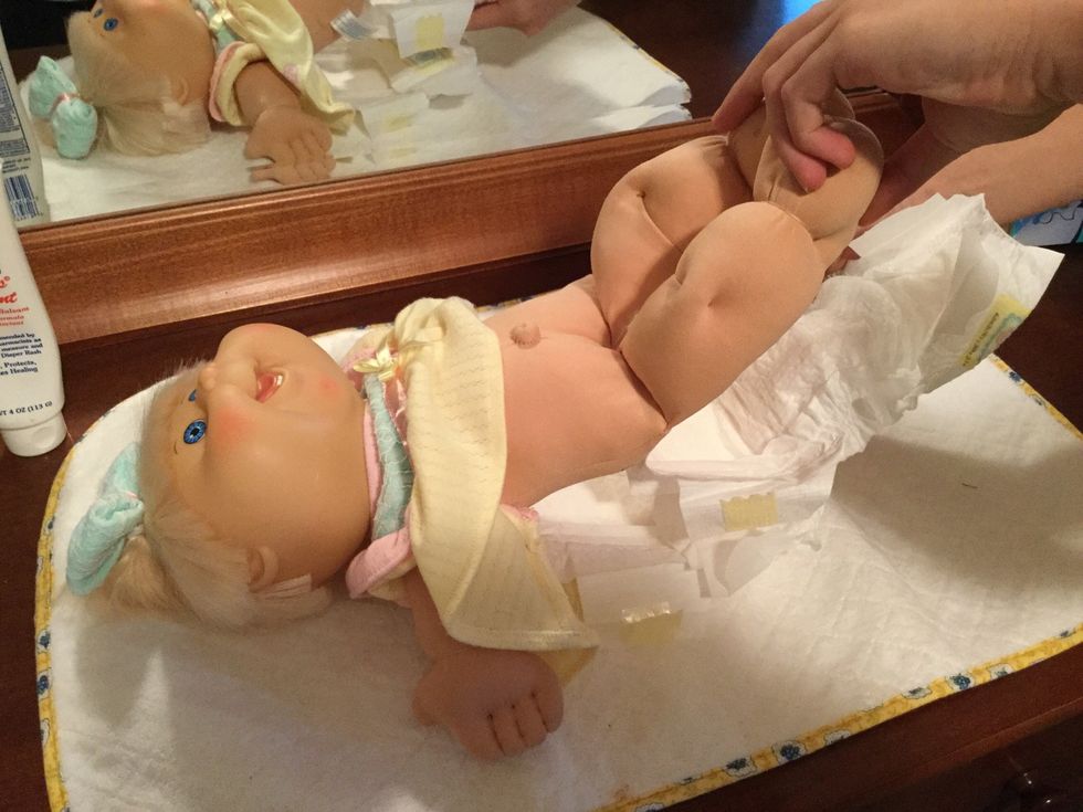 After everything has dried, grab the child's legs and gently lift their bottom off the surface and slide the clean diaper under. When the clean diaper is fully placed under, remove the dirty diaper.
