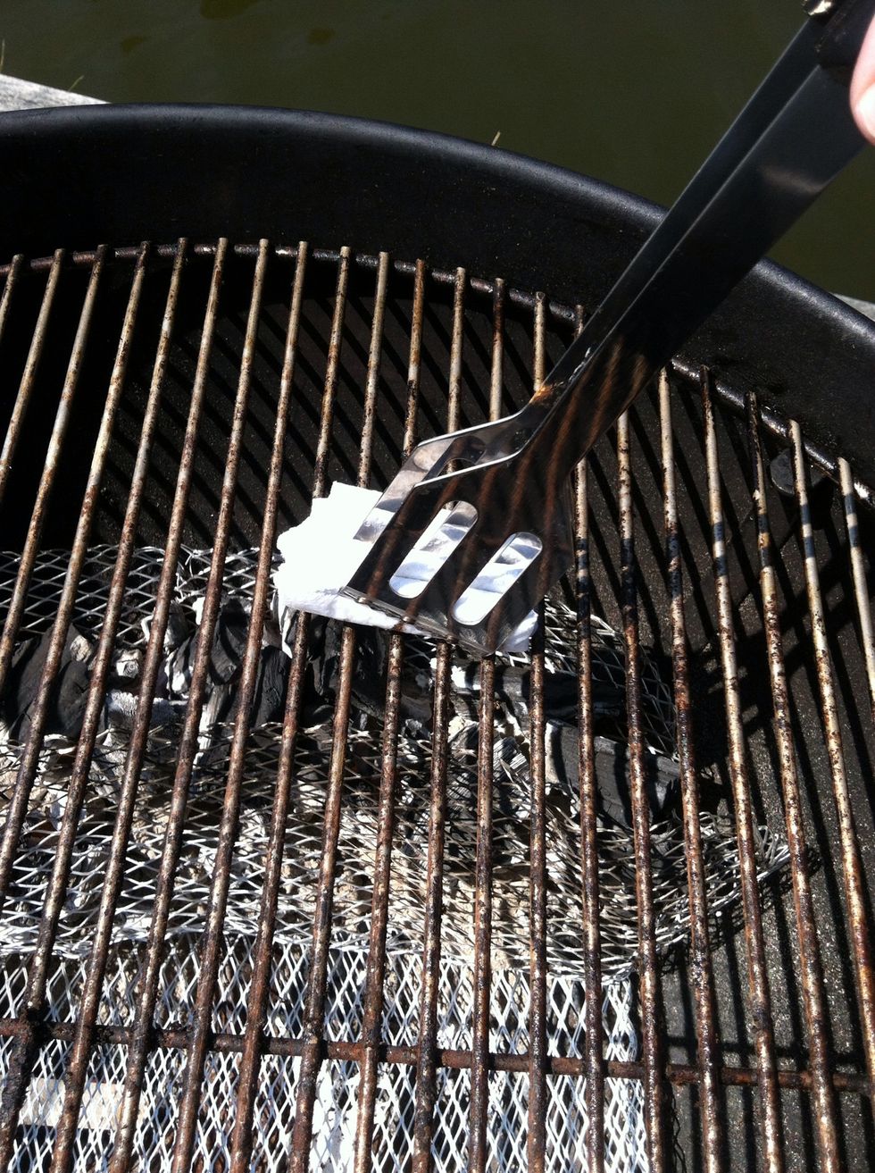 After scrubbing the grill surface with a wire brush, grip a tightly-folded paper towel with the tongs.  Dip it in some vegetable or canola oil and draw it across the grill grate to prevent sticking.