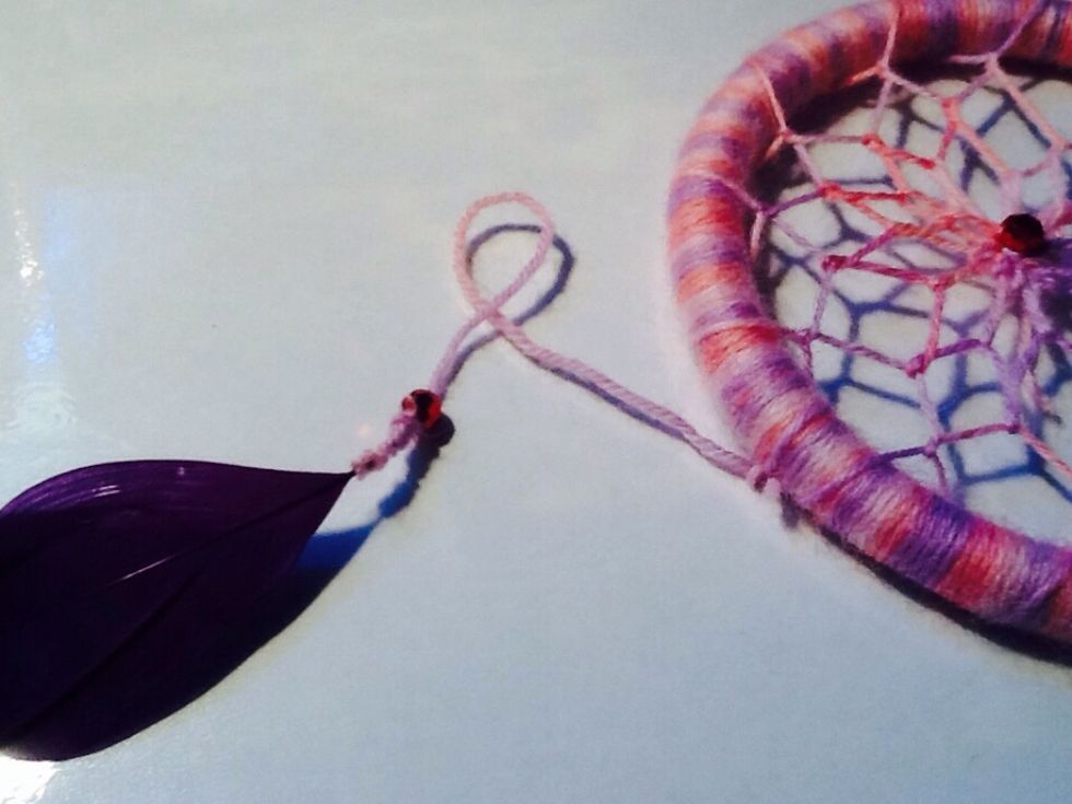 After wrapping around the stem of the feather, and threading a bead through, tie a knot at the base of the bead. Then attach the whole piece to the bottom of your hoop.