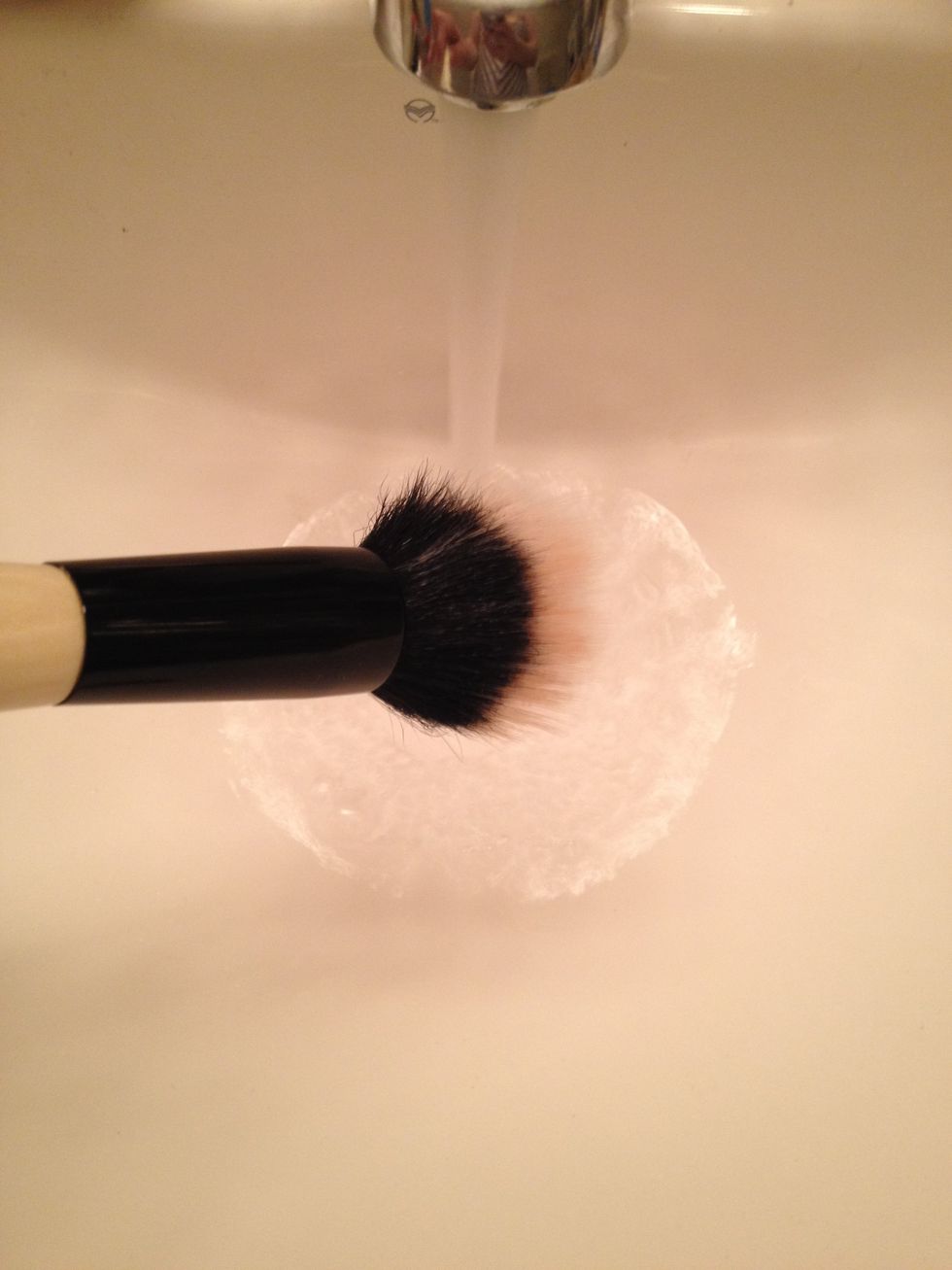 Angle your makeup brush DOWNWARD into a stream of LUKEWARM water.  This prevents water from seeping into the barrel, which will over time, loosen the glue and ruin your makeup brush.