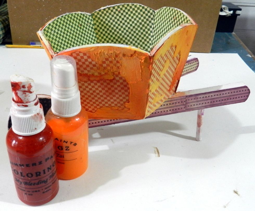 Apply crackle paste on some places of the wooden wheelbarrow and after dried, apply orange glimmer spray.
