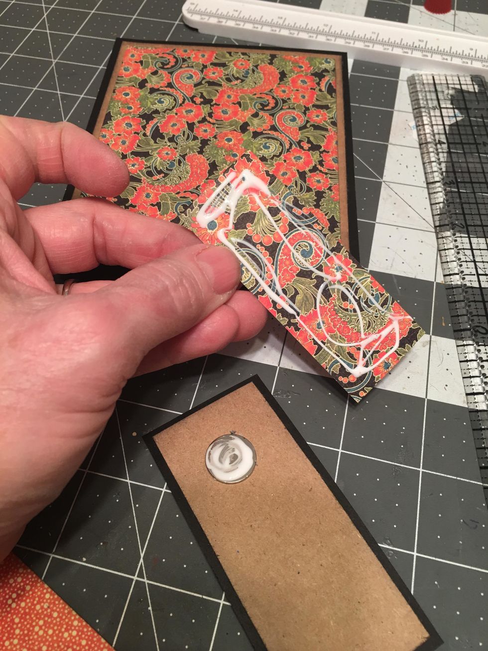 Apply glue to the magnet as shown and the back of one of the patterned papers for the closure. Center and attach down on to the closure piece covering the magnet. Burnish well.