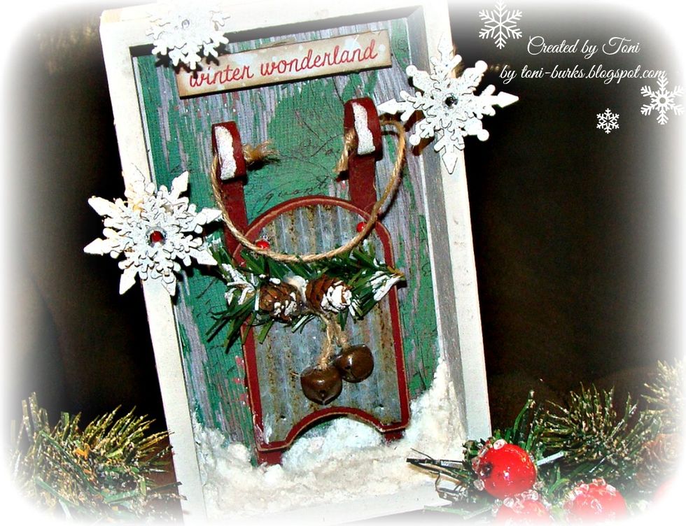 Apply some to your greenery and sled as well. Layer your snowflakes on top of each other and glue to the outside of the box, and add gems to the center.