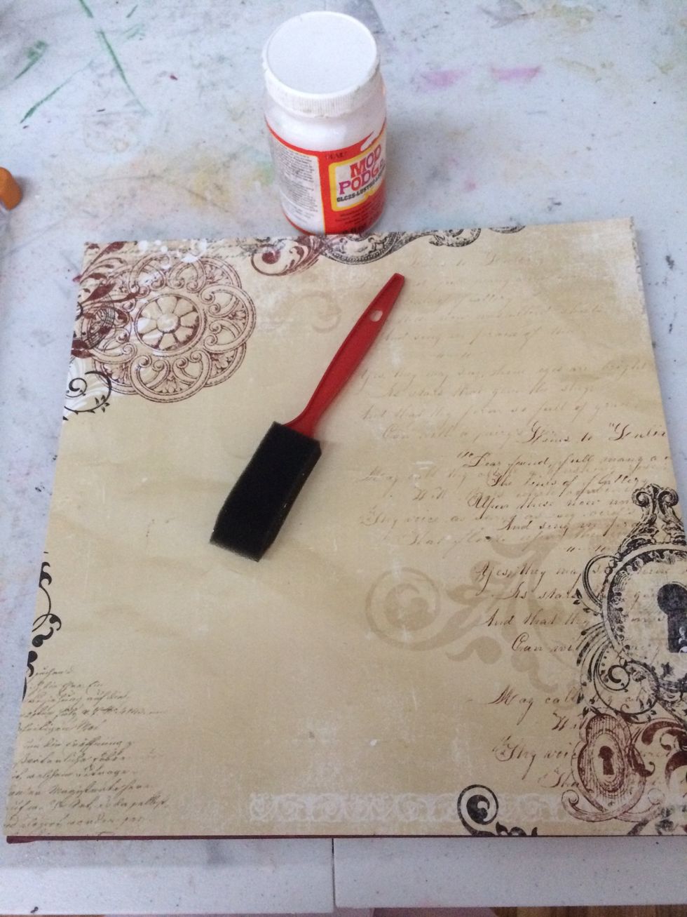 Apply the paper to the canvas with mod podge. Don't panic if you have bubbles, just be patient and let it dry. The project will have a lot of texture so small imperfections won't be noticeable.
