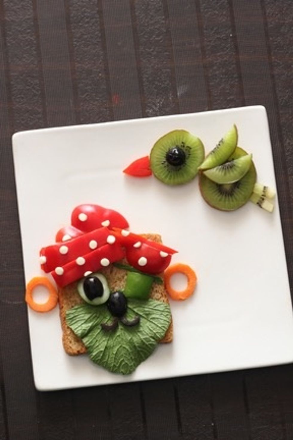 Arrange the 2whole slices of kiwi for parrots body , and halves and strips for the wings and feet respectively. Finally place the bell pepper beak and olive eye to complete the look.