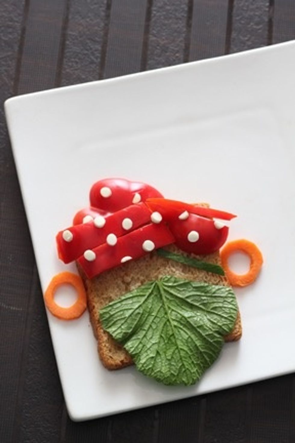 Arrange the cheese polkas , carrot ear rings and radish greens beard and eye patch strip on the bread face.