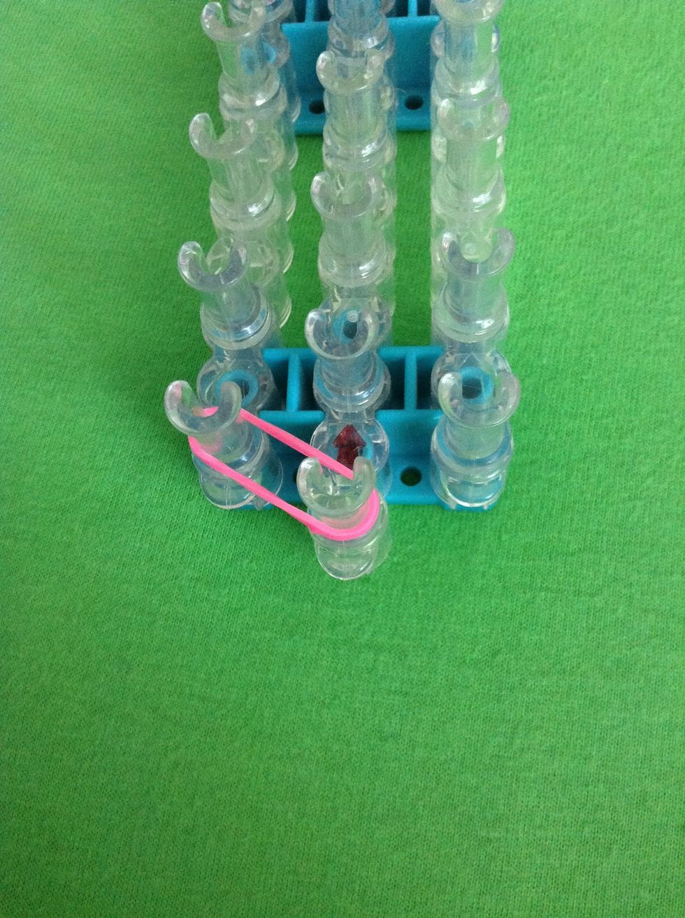 Arrange your loom with arrows pointing away from you and the middle row in front of the sides. Stretch a rubber and from the middle to the left side.