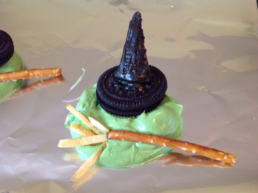 Assemble: pour the green-colour white chocolate into a puddle for the melted witch. My chocolate wasn't soft enough here. Quickly add the hat and make a broom out of a pretzel and hickory sticks.