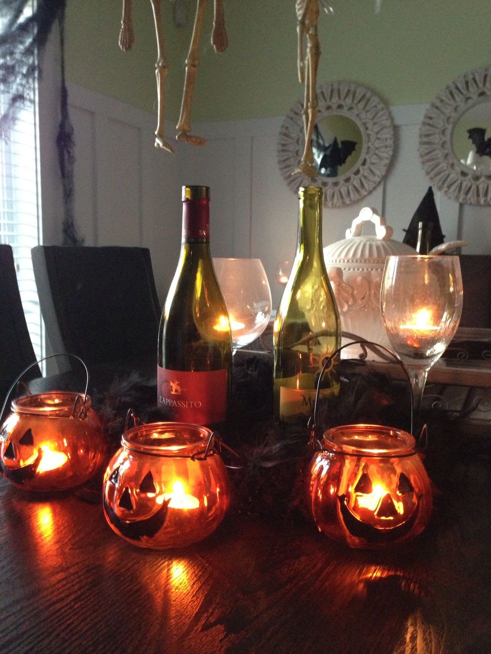 At each end of your chosen centrepiece, add one black feather boa, 3 wine bottles, 2 wine glasses and 3 glass pumpkin lanterns with votives. Balance at each end will make your table look complete.
