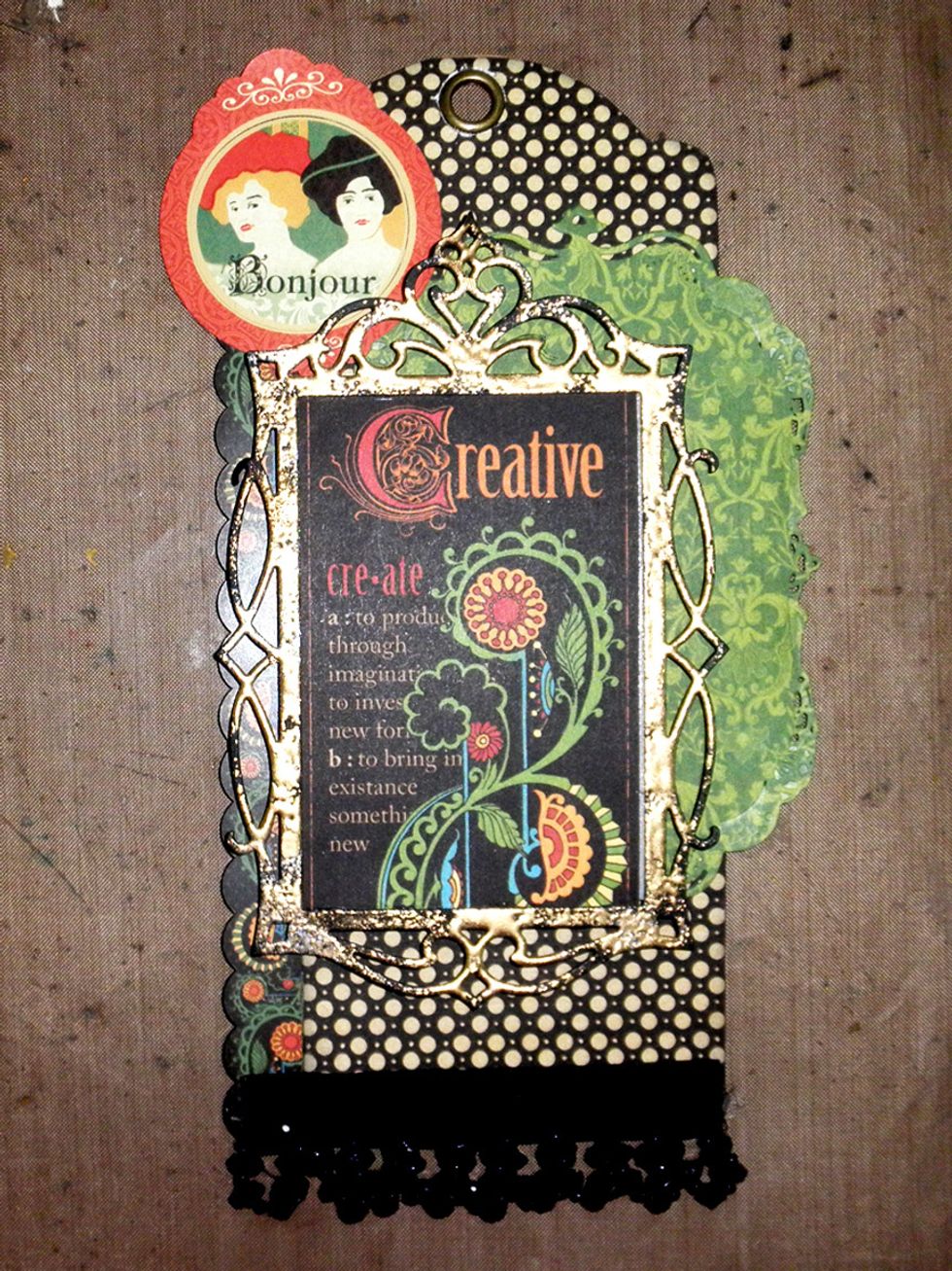 Attach the frame to the tag as shown.  Here you can see that the black frame shows thru the embossing in places to add to the aged look.  Adhere a 4" strip of beads or trim at the bottom.