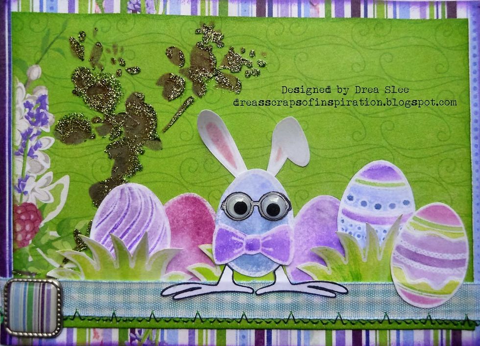Attach the striped brad to the left side of the ribbon, and glue down another egg to the right. Stamp bunny feet with black ink, fussy cut, and glue to the bottom of the center egg.