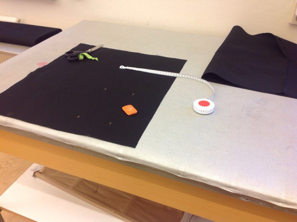 Av den lilla biten som blir \u00f6ver ska du klippa tv\u00e5 handtag. M\u00e4t 10cm fr\u00e5n kanten och klipp en remsa som \u00e4r lika l\u00e5ng som tygbiten. G\u00f6r en likadan till.