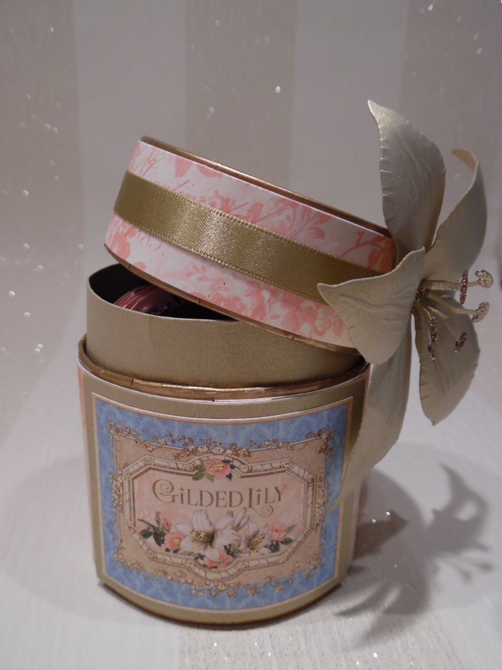 Band of card used to form lip between the two halves. Ribbon added to the lid. Flower cut from card with Sheena Douglas die. Petals curled by hand and detail added with embossing tool.