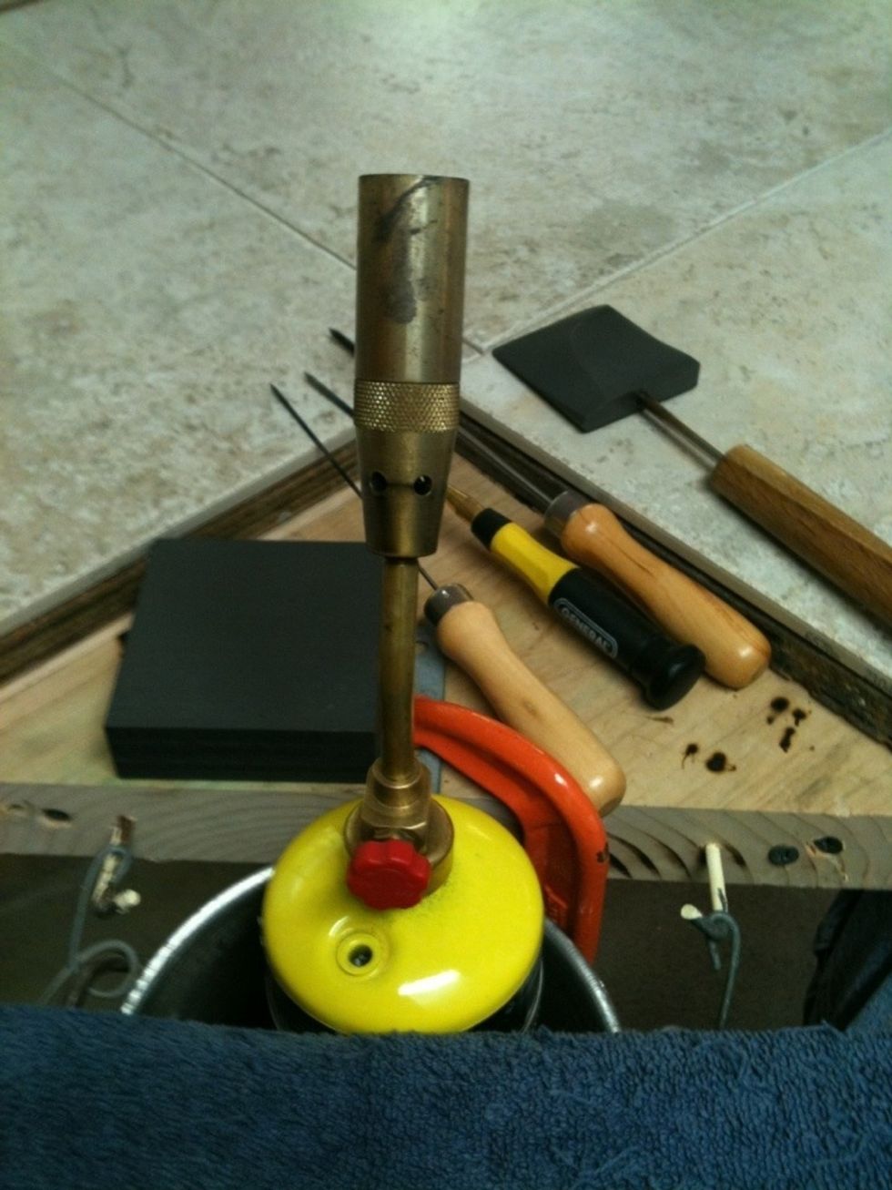 Basic "Hot Head" torch, uses MAPP gas canisters. Black block on left is graphite marver, 3 hand tools are pokers, rightmost is graphite tool. Worktable surfaced with ceramic fireproof floor tiles.