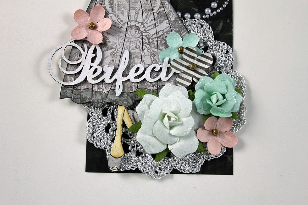 Begin adding flowers to the tag as shown. Paint chipboard title using white acrylic paint. Adhere to the bottom of the dress.