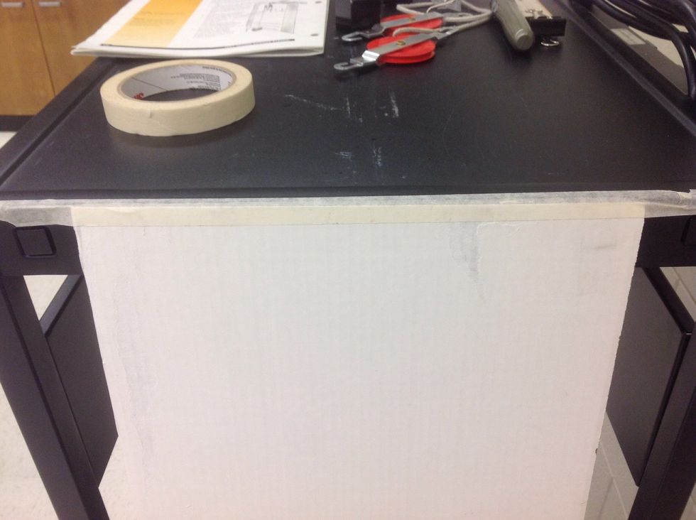 Begin by attaching the 30 cm  x 50 cm sheet of cardboard to your table using the masking tape.  Cut a piece long enough  (30 cm) to attach the entire top of the cardboard.