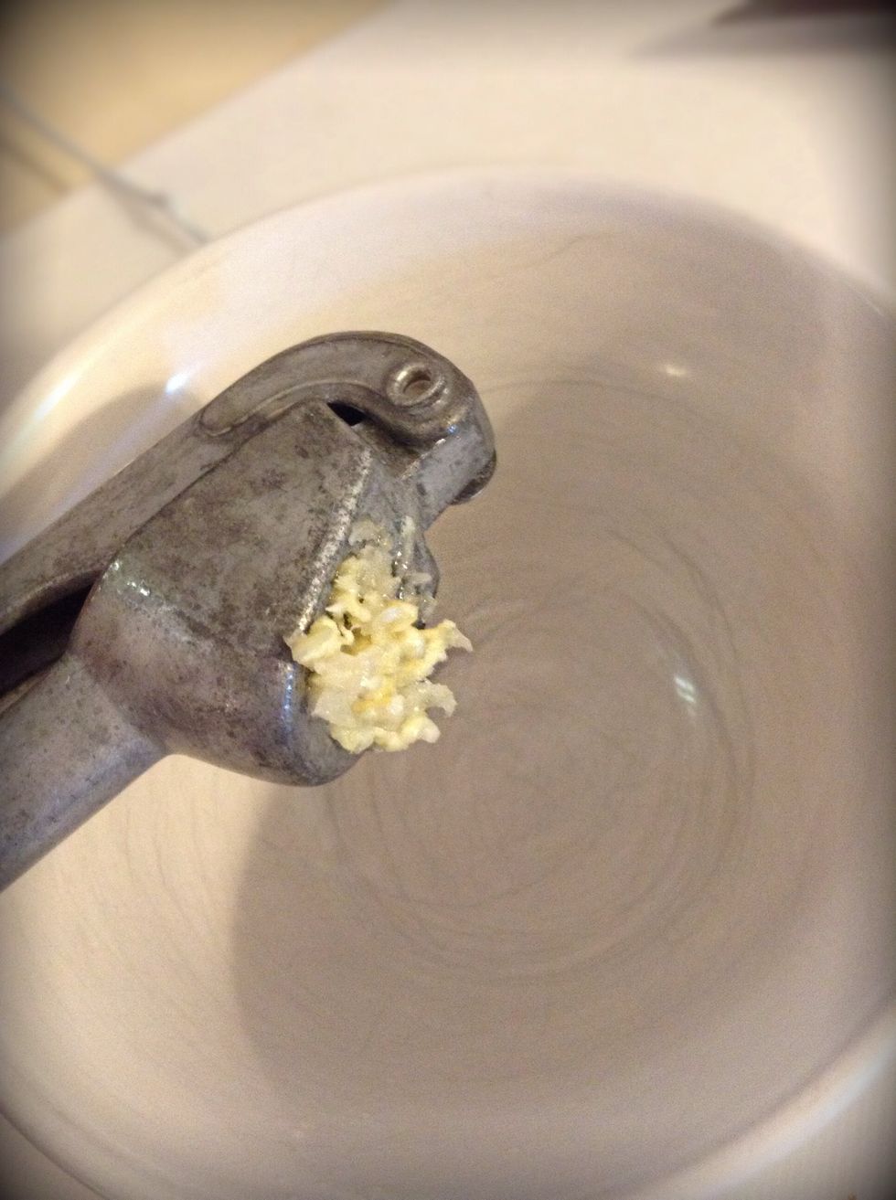 Begin to crush your garlic cloves. I use a garlic press which works great. Place both cloves of garlic in with the 3 tablespoons of fresh parsley.