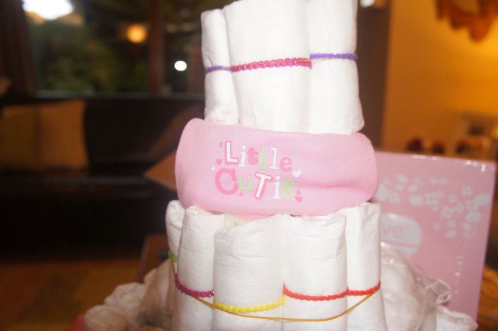 Begin to decorate your Nappy Cake with vests, bibs, swaddle blankets or whatever you like! I found/made little gaps in and around the nappy stacks to place in vests etc.