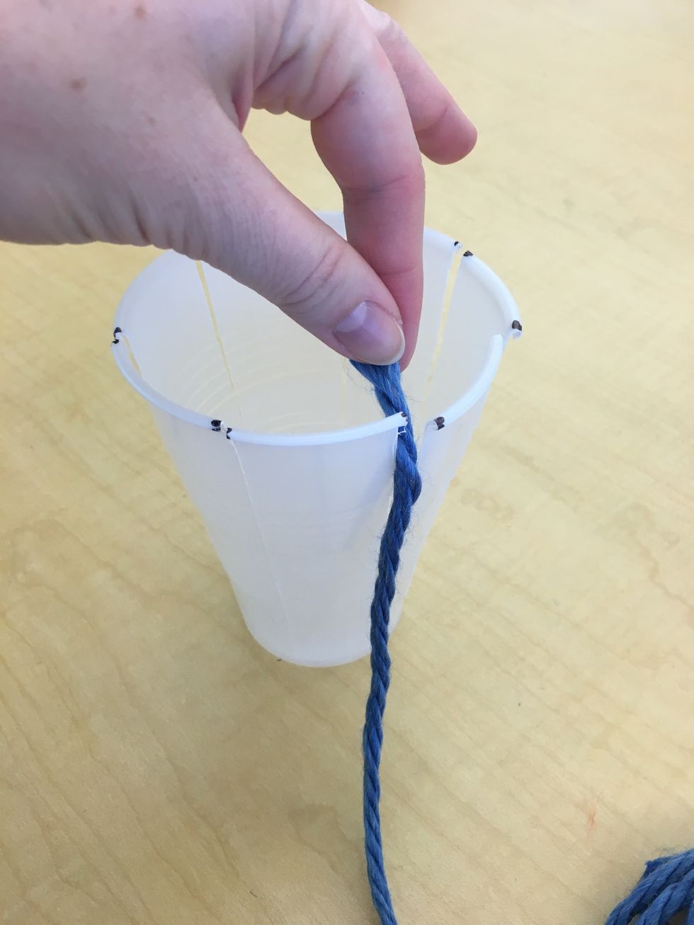 Begin your weave by taking the end of the piece of yarn and slipping it in through the top of one of your warp pieces. Remember! WARP goes up and down!