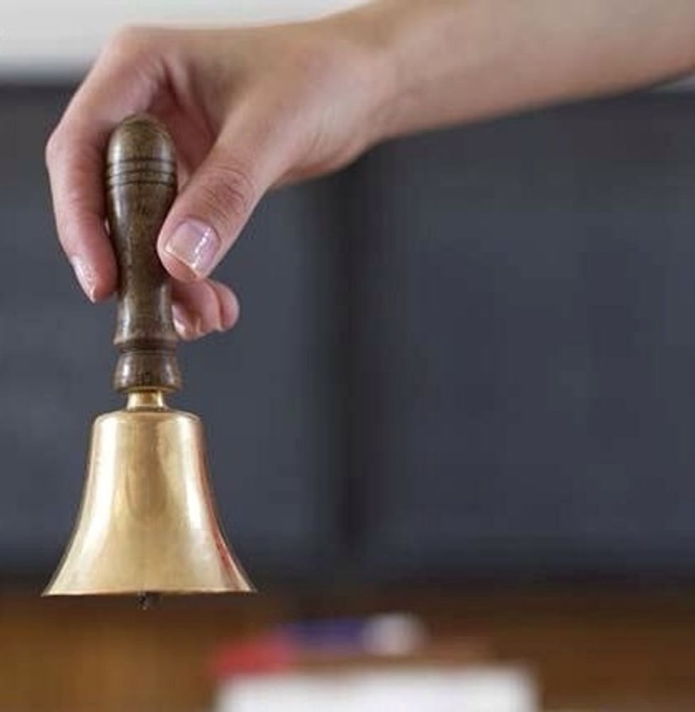 Bell is on the floor in front of the seated child. Child stands up, bends over and  carefully (without allowing it to ring) carries the bell to someone sitting across from him, and places it on floor.