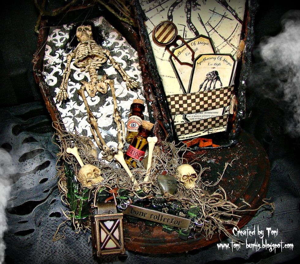 Bend your fence up and down and glue into place, tuck moss here and there for interest. Add your bones, vials, and skeleton heads. Comment