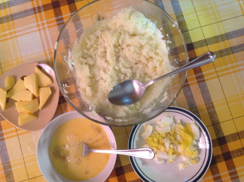 Boil the potatoes and mash it up in a large bowl together with the diced cheese. Mash one hardboiled egg and mix it with the mashed potato. Beat the remaining eggs and mix and mix together.