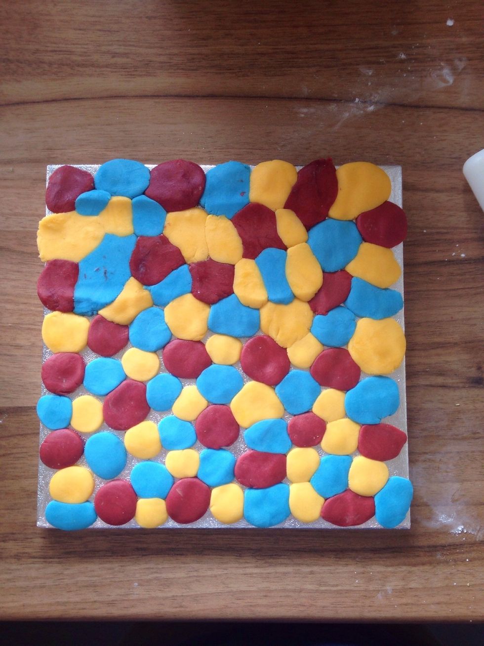 Brush your cake board with water and cover it with small balls of different coloured fondant, don't worry about the gaps