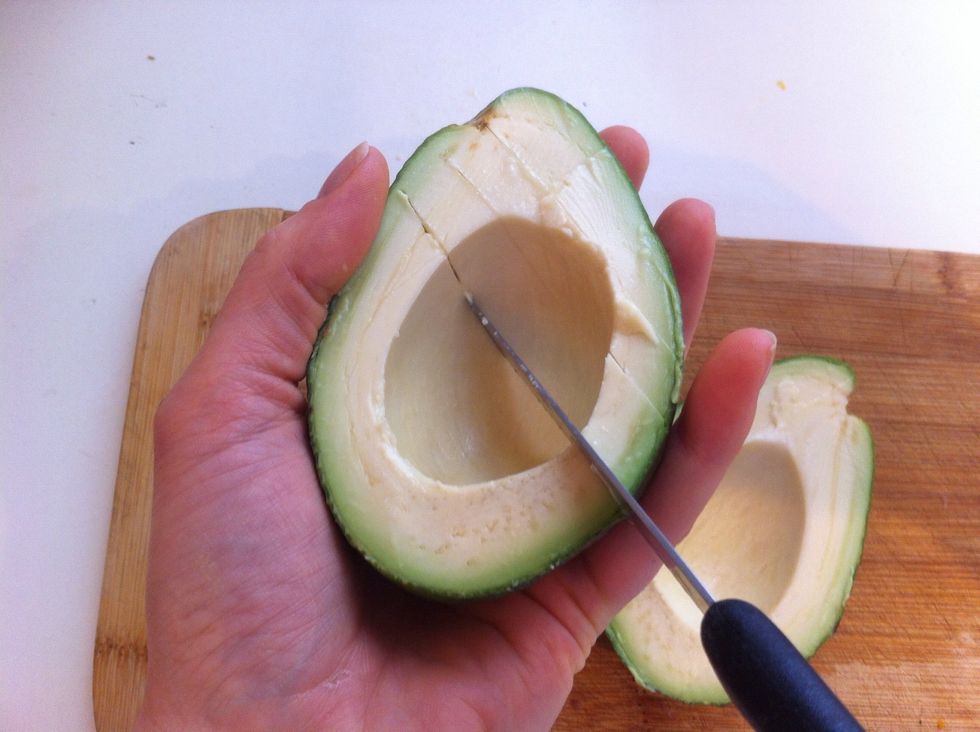Carefully! Hold the avocado in one hand, cut the flesh into strips, go gently so you don't pierce the skin or yours! A blunt knife is a good idea when starting out!