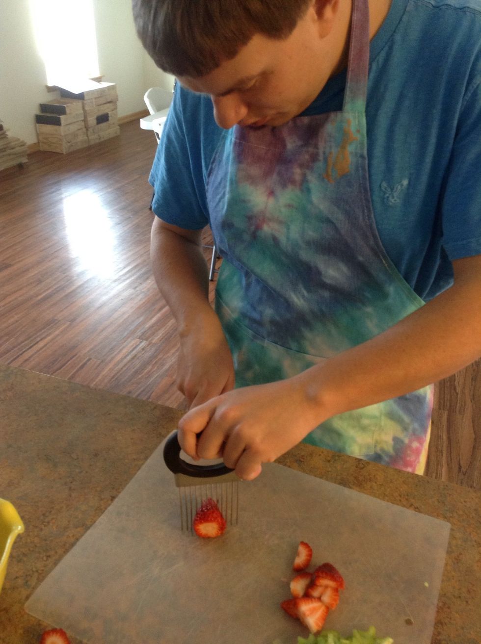 Carefully using cut guiding tool, knife, and cutting board slice the strawberries into thin slices