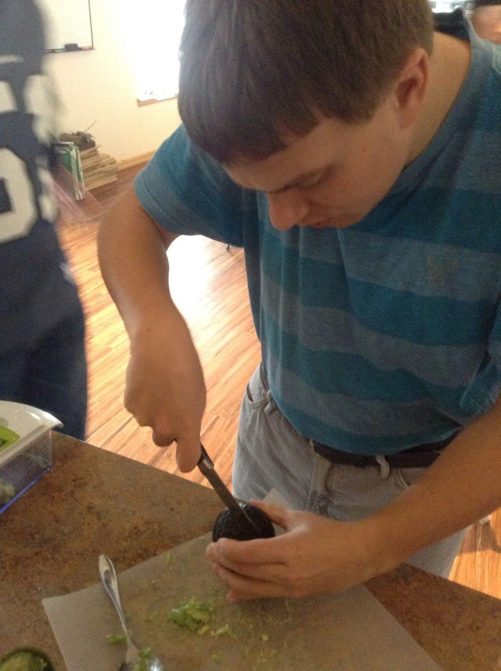 Carefully using cutting board and knife cut the avocado in half