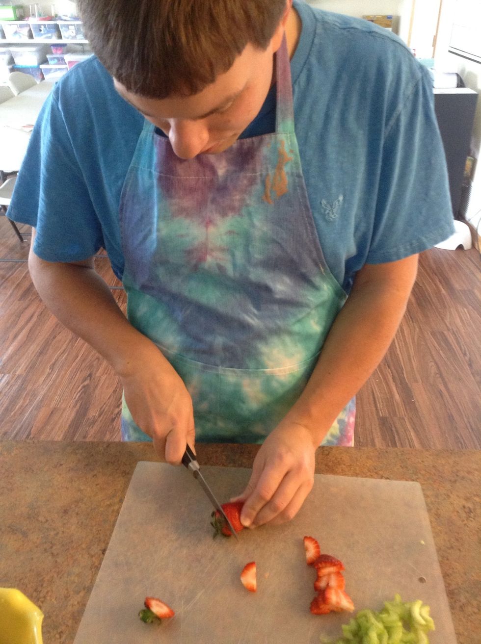 Carefully using cutting board and knife cut the tops off of strawberries
