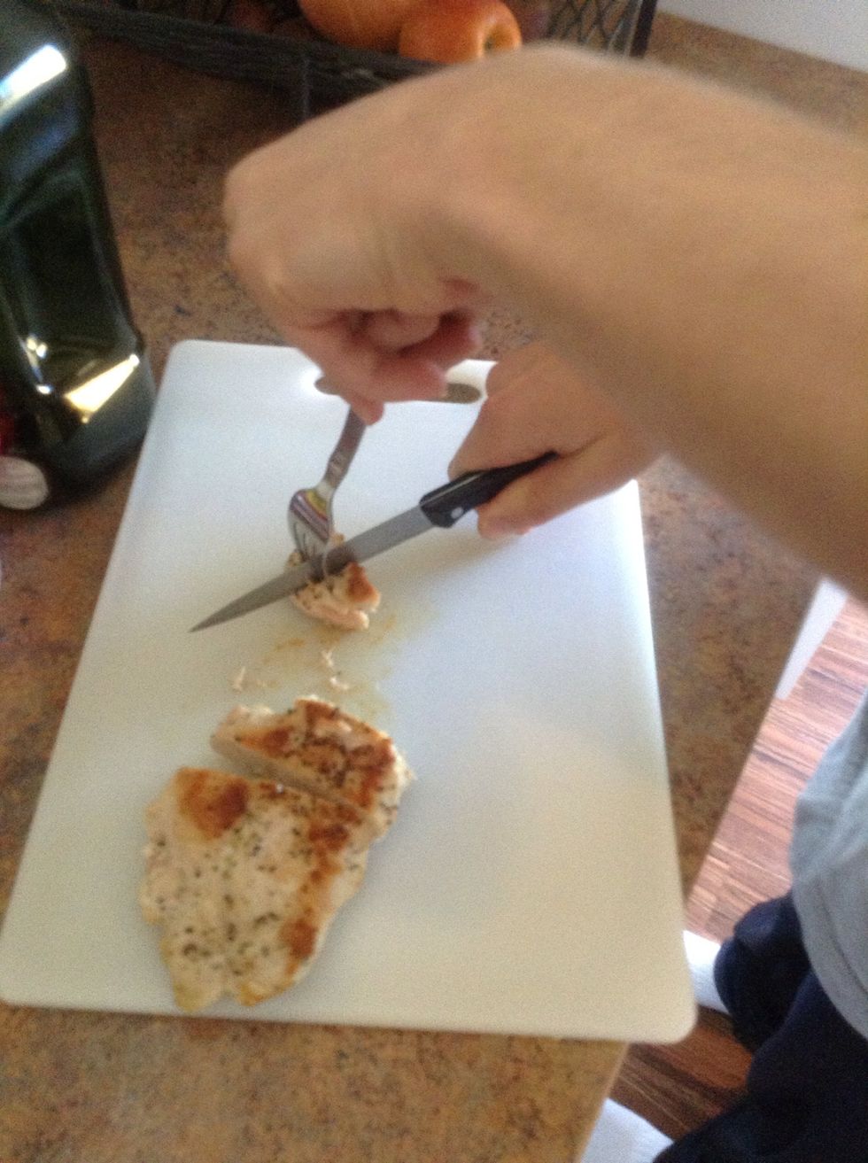 Carefully using cutting board,fork, and knife cut the chicken into bit sized pieces.