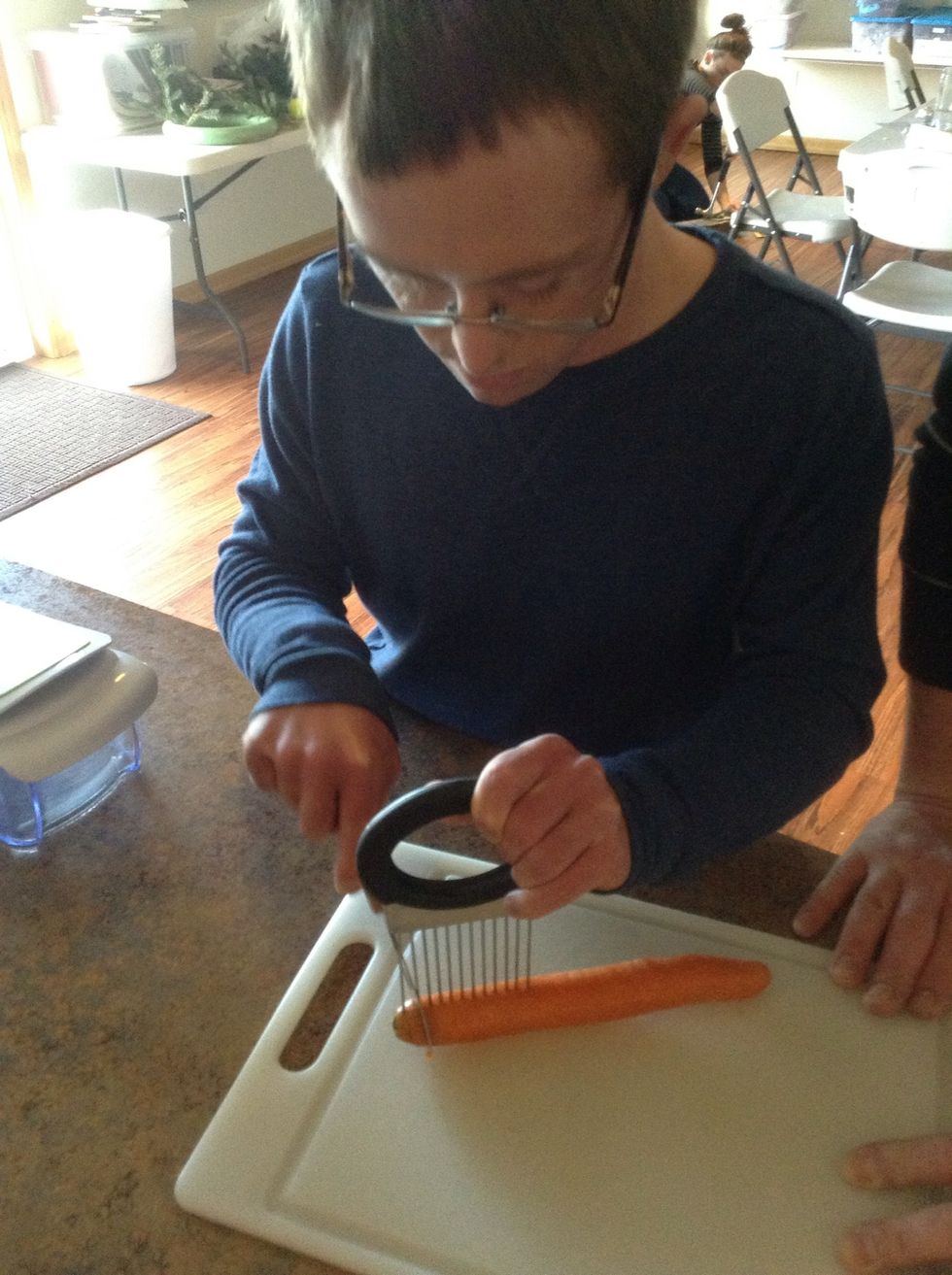 Carefully using knife, cutting board, and cutting tool cut the top off the carrots