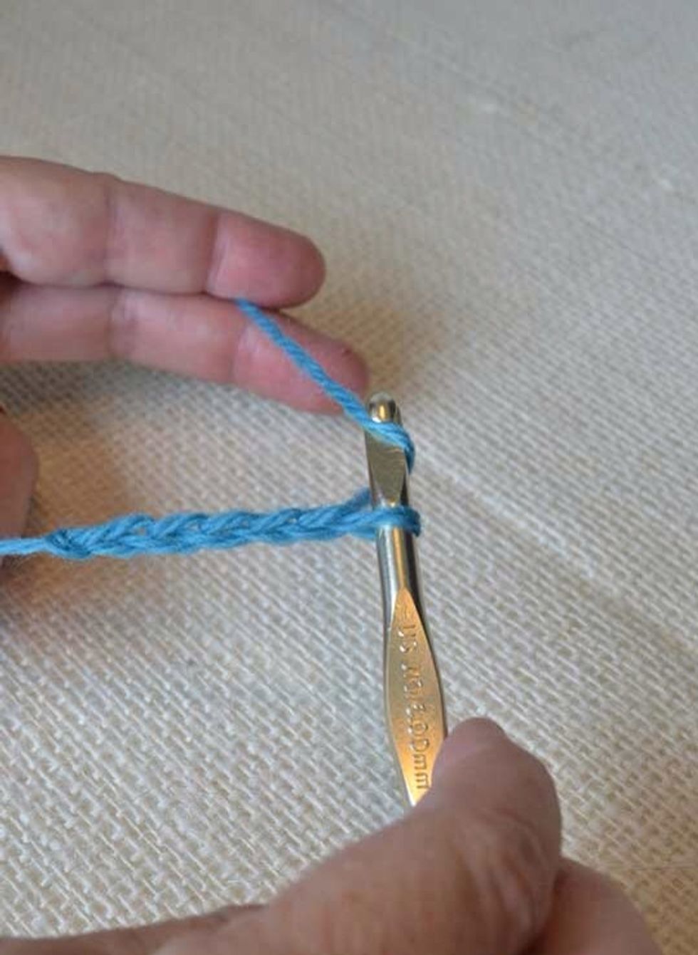 Catch the yarn with the hook & draw it through the loop on the hook, pulling toward you & leaving the new loop on the hook instead. Repeat this until you have a foundation chain of about 5-7 stitches.