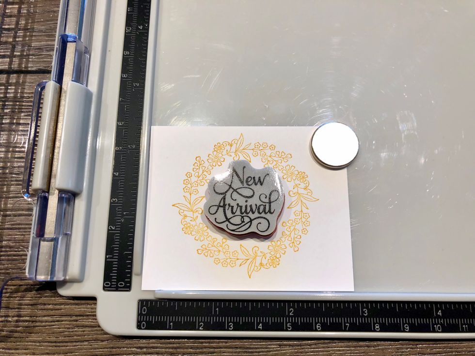 Center the New Arrival stamp in the center of the wreath and stamp with the same ink.