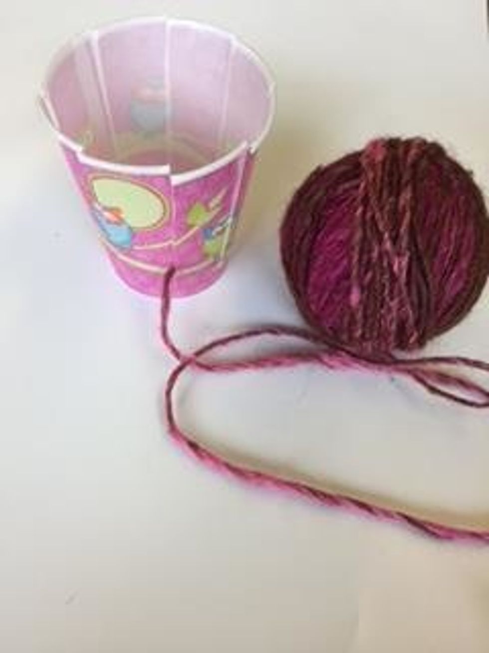 Choose a color of yarn. Begin by pulling the strand of yarn through one if the slits in the cup, all the way to the bottom of the slit.