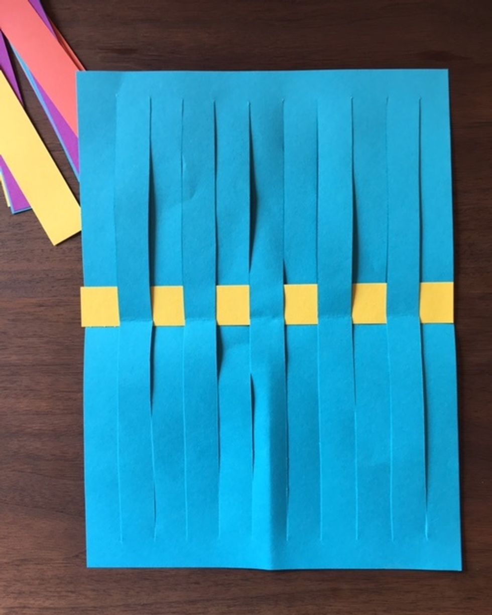 Choose a paper strip color you would like to weave through the warp lines. The paper strip is called the weft. Use an ABAB pattern to weave weft through warp lines. Weave through center of loom.
