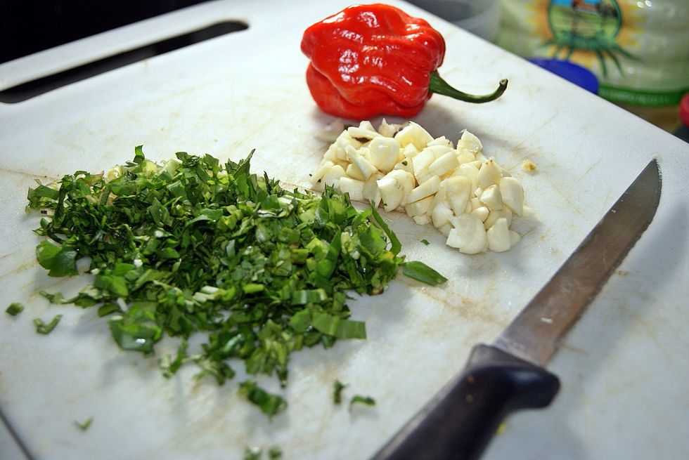 Chop garlic except for 4 or 5 cloves. Chop shadon beni (cilantro) too. Put the hot pepper close by to make onlookers think the curry is going to be good because it's colorful. Yuh don't have to but...