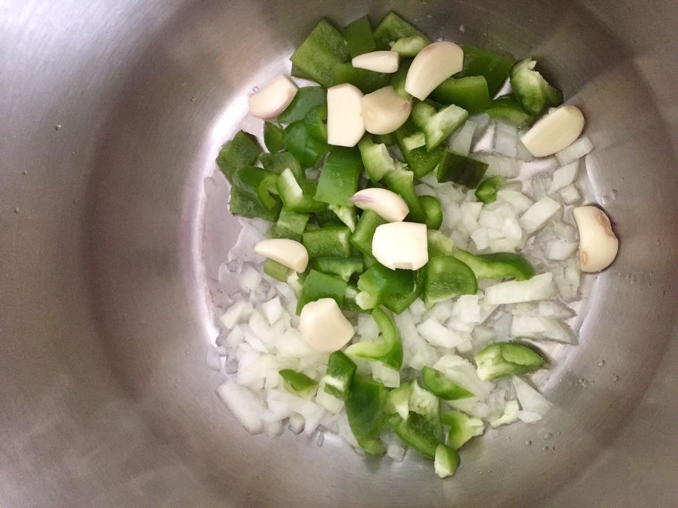 Chop the onion and the pepper and start cooking in a bit of oil. Peel the garlic cloves but leave them whole and add them too