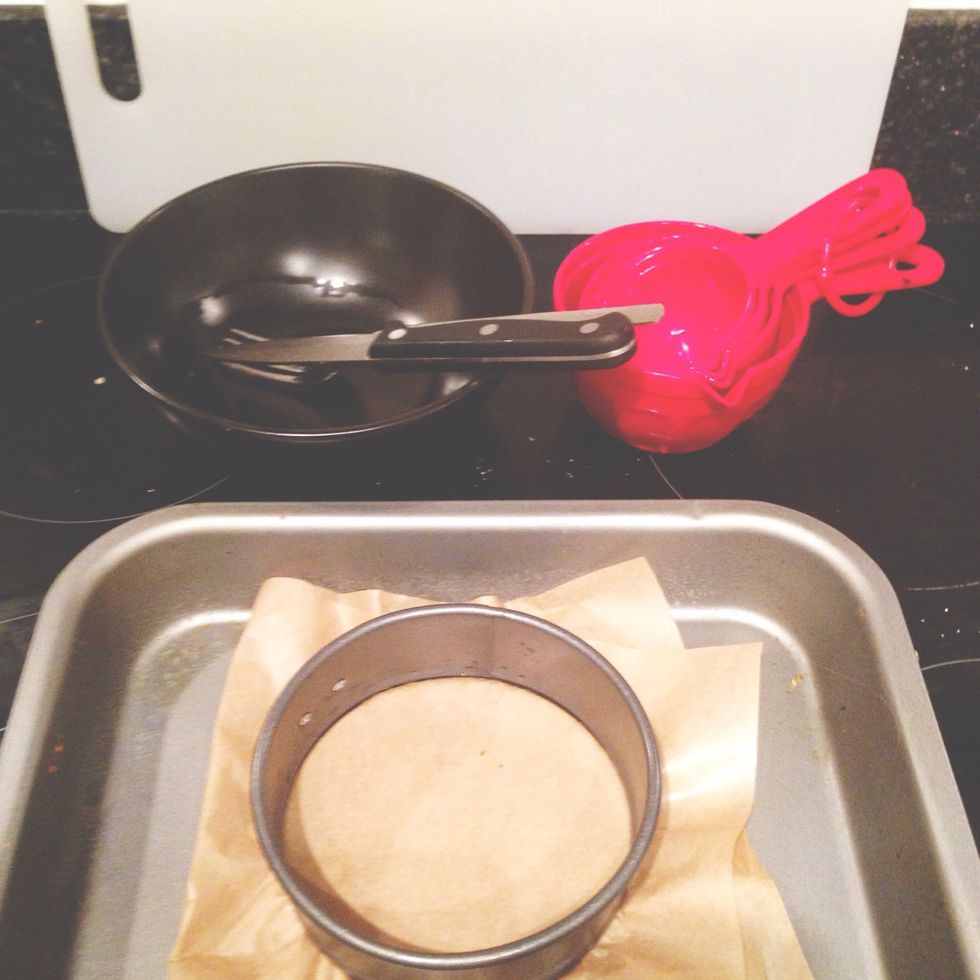 Chopping board, measuring cups, bowl, fork, chopping knife, tin, baking tray, brown greaseproof baking paper
