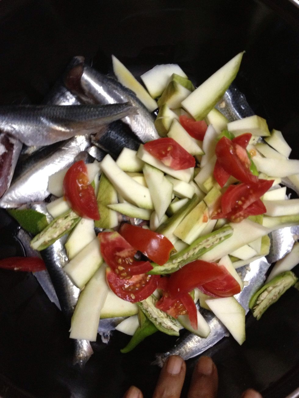 Clean the fish, then add to a bowl, then add slicedraw mango, sliced tomatos, slitted green chillies