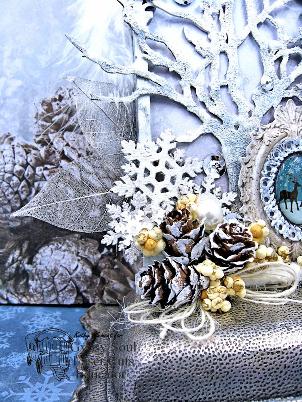 Cluster small pine cones and berry picks in the left hand corner of the frame.  Glue prepared snowflakes behind the pine cones.  Tie a loop bow from ivory burlap string and blue in place.