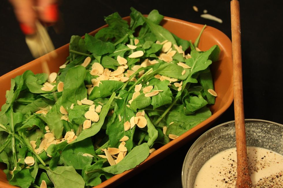Coloque as folhas verdes numa saladeira. Espalhe as am\u00eandoas fatiadas.