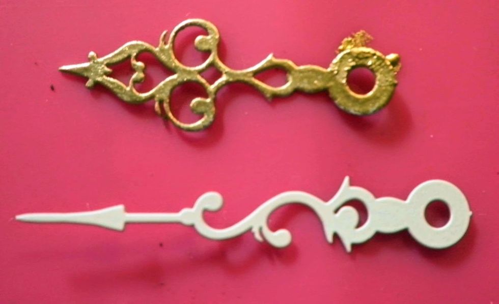 Color white metal clock hands with Krylon gold leaf pen. Punch hole in center of clock face, add clock hands with decorative brad and gold bead to center.