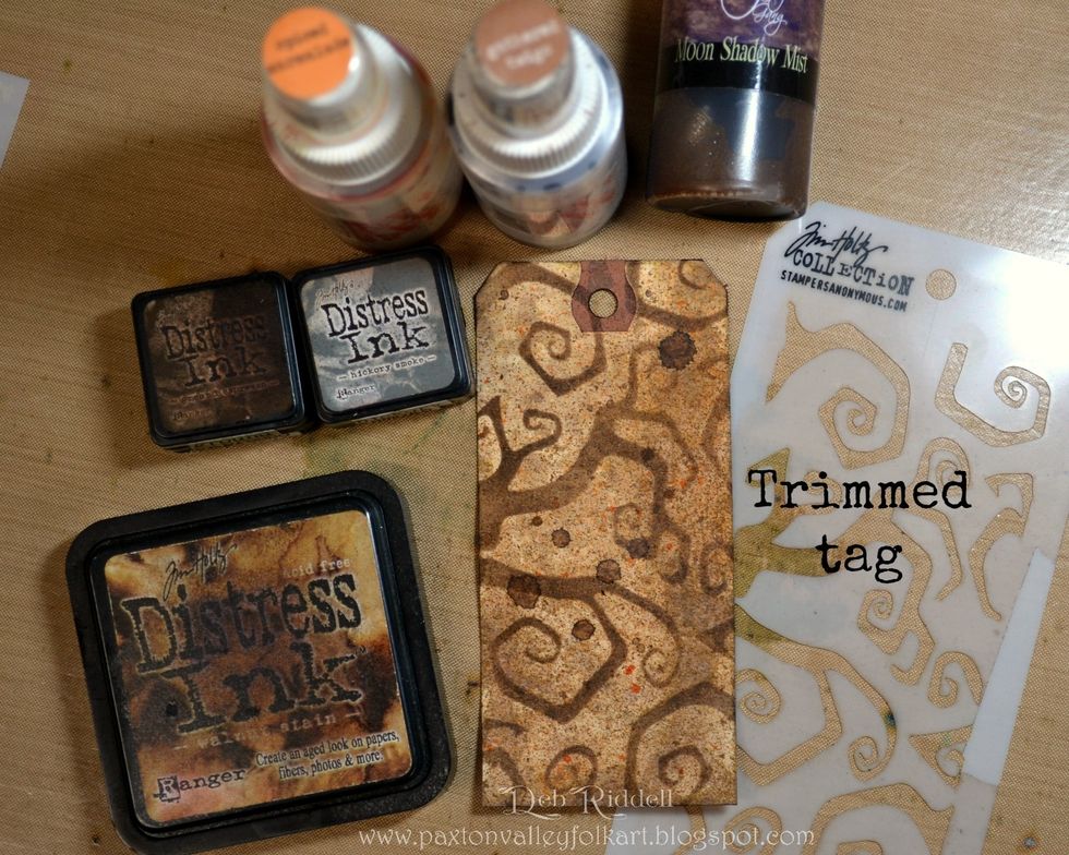Colour the two trimmed tags with Distress inks (Walnut Stain, Ground Espresso, Hickory Smoke) and then spray lightly with Distress spray stain (Gathered Twigs & Spiced Marmalade) front and back.